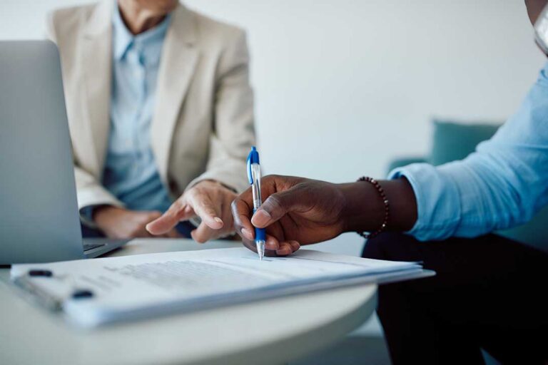 A person reviews home insurance paperwork with a house and laptop visible on the table.