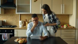 A couple reviews life insurance papers beside medical records and a calculator at a kitchen table.